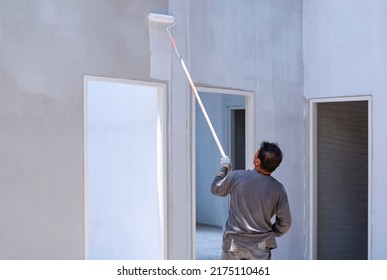 Asian Builder Using Long Handle Roller Brush To Painting Primer White Color On Concrete Wall Inside Of House Construction Site