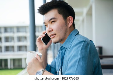 Asian Business Man In Blue Collar Shirt Talking On The Phone At Hotel Balcony.