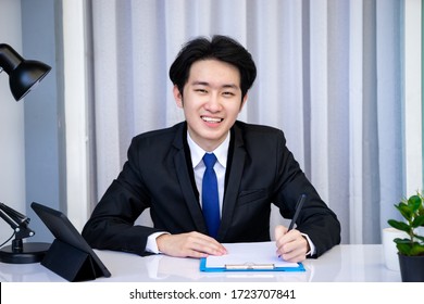 Asian Business Man Dringking Coffee Wearing Suit, Enjoying Watching Educational Webinar On Laptop Or Laptop And Smartphone. Smiling With Chat And Holding Video Call With Clients Partners.