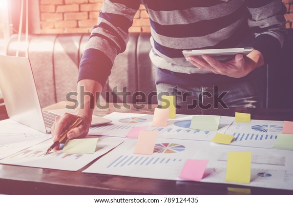 Asian business man hand holding note paper\
meeting with new startup project use post it notes to share idea\
discussion and analysis data charts and graphs.Business finances\
and accounting concept\
