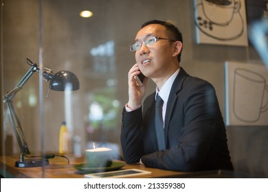 Asian Business Man Having Coffee And Phone Conversation At Cafe