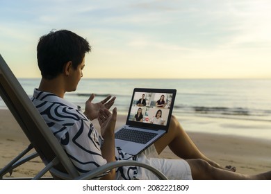 Asian business man having remote video conference call with his business team at the beach during vacation in holiday.