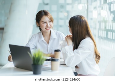 Asian business man present and explain work to female colleague, using laptop computer in office at night. Teamwork, coworker cooperation, financial marketing team, or corporate business concept. - Shutterstock ID 2124824630