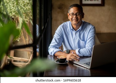 Asian Business Man Smiling.Small Business Owner Relaxing In Vintage Cafe,drinking Coffee.Working Online Concept