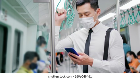 Asian Business Man With Surgical Mask Face Protection Use A Smartphone  And Keep Social Distancing To Crowd While Commuting In The Metro Or Train