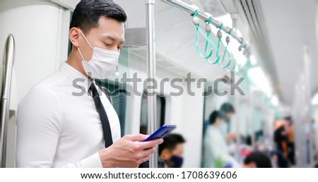 Asian business man with surgical mask face protection use a smartphone  and keep social distancing to crowd while commuting in the metro or train