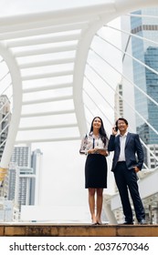 Asian Business Man Talking On Mobile Phone And Young Beautiful Woman Working On Digital Tablet Computer Standing Outside Office Building.