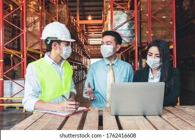 Asian Business Man, Woman And Engineer Wear Protective Face Mask Talk With Laptop Computer In Warehouse Cargo. Concept Of New Normal Work In Industry, Cargo During Covid 19 Corona Virus Pandemic.