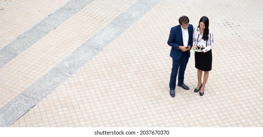 Asian Business Man And Young Beautiful Woman Working On Digital Tablet Computer Standing Outside Office Building.