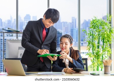 Asian Business Manger And His Female Secretary Wearing Formal Suit Are Discussing Over The Annual Report In Formal Business Office With Cityscape