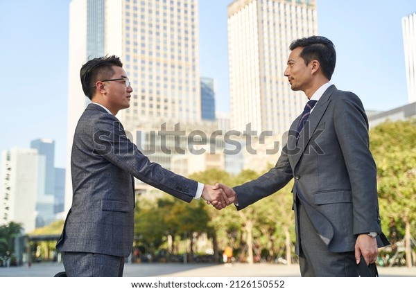 asian\
business men meeting outdoors shaking\
hands