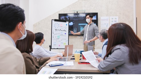 Asian Business Team Wear Facial Mask In A Meeting And A Young Male Leader Emphasize The Importance Of Teamwork