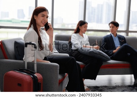 Asian business who using mobile phone with trolley luggage sitting on the sofa in airport lounge