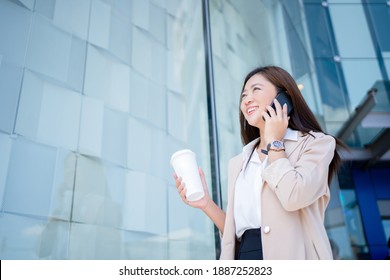 Asian Business Woman Drinking Coffee And Talking On The Phone While Walking Outdoors.