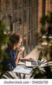 Asian Business Woman Drinking Coffee And Working On Laptop In Cafe