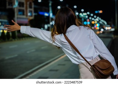 Asian Business Woman Hail Waving Hand Taxi On Road In City Street At Night, Beautiful Woman Smiling Using Smartphone Application Hailing With Hand Up Calling Cab Outdoor After Late Work, Back View