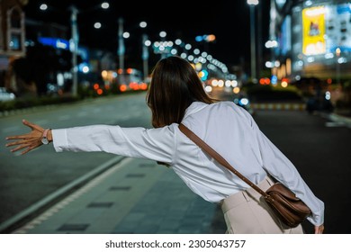 Asian business woman hail waving hand taxi on road in city street at night, Beautiful woman smiling using smartphone application hailing with hand up calling cab outdoor after late work, back view - Powered by Shutterstock