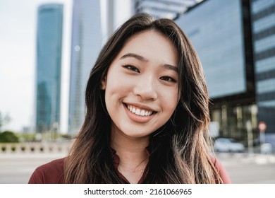 Asian business woman looking at camera outdoor with office buildings on background - Focus on face