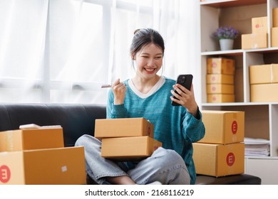 Asian Business Woman On Sofa Using A Laptop Computer Checking Customer Order Online Shipping Boxes At Home. Starting SME Small Business Entrepreneur Freelance. Online Business, SME Work Home Concept.