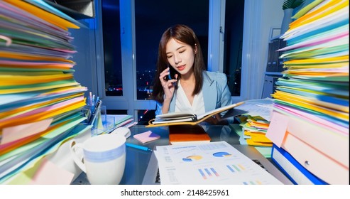 asian business woman overtime work with stack of documents and speak on phone in office at night - Shutterstock ID 2148425961