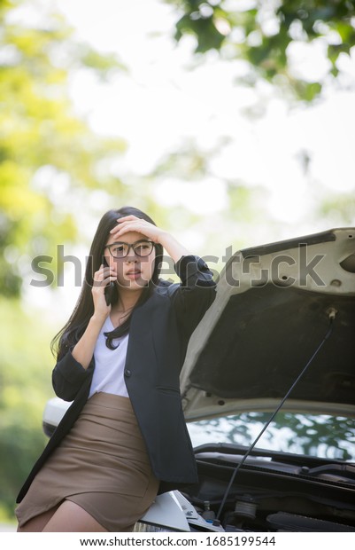 Asian business woman sad\
waiting for help by a broken car. Use a mobile phone to call the\
mechanic.