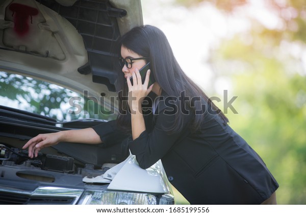 Asian business woman sad\
waiting for help by a broken car. Use a mobile phone to call the\
mechanic.