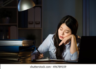 Asian Business Woman Sitting At Desk Sleepy Working Overtime Late Night. Indoors Office Background