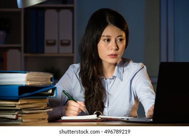 Asian Business Woman Sitting At Desk Working Use Laptop Overtime Late Night. Indoors Office Background