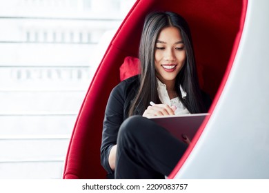 Asian Business Woman Sitting Inside Ball Chair At Office Drawing On Digital Tablet