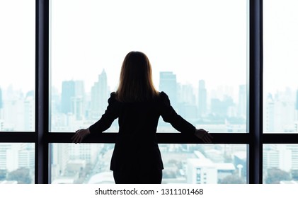 Asian Business Woman Standing And Looking Out The Window At City View Background