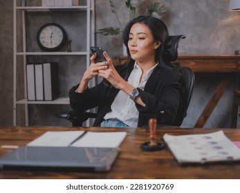 Asian business woman is using smartphone for searching or watching social media to entertain while breaking time at workplace. Female manager is chat with her friend during break time. Online shopping
