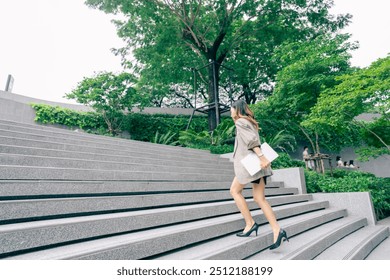 Asian business woman walking to work diligently and briskly in morning in a big city. female in a business suit, dressed in a smart suit, runs to work during rush hour in corridors and stairs. - Powered by Shutterstock