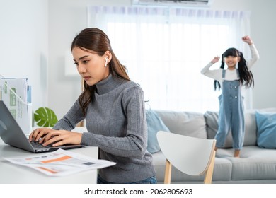 Asian Business Woman Work At Home With Young Kid Daughter Play Around. Attractive Beautiful Mother Loss Concentration On Job In Laptop Computer And Feel Frustrated From Children Making Noise In House.