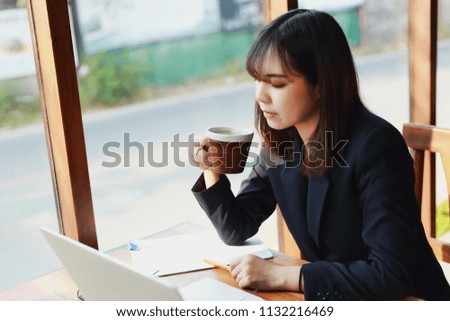 Asian business woman working in in coffee shop cafe with laptop paper work hand Holding coffee   (Business woman concept.)
