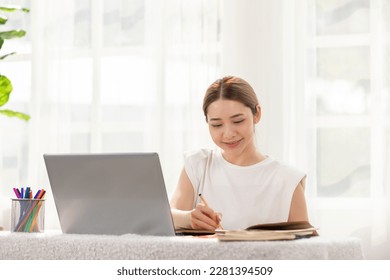 Asian Business woman writing down requirement and ideas to book for planing Business Startup,Feeling so happiness and working with positive emotional,Small Business Startup Concept - Powered by Shutterstock