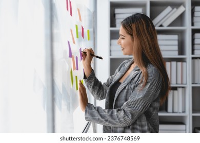 Asian business woman writing something on sticky notes while working on a business plan at office. - Powered by Shutterstock