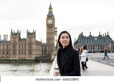 Asian Business Women Holding Cup Of Coffee Near Big Ben, London, England. Girl In London During Winter Near Westminster Bridge, London. Business Woman Model With Coffee.