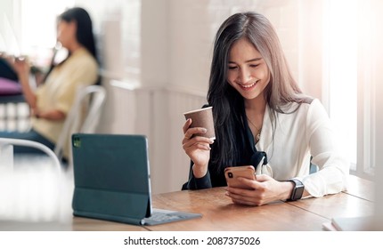 Asian Business Women Sitting At Cafe Or Office And Drink Coffee Looking At Smartphone.