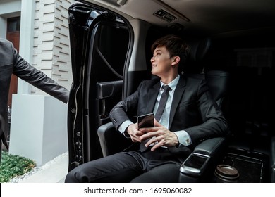 Asian businessman arriving at destination, chauffeur opening car door.