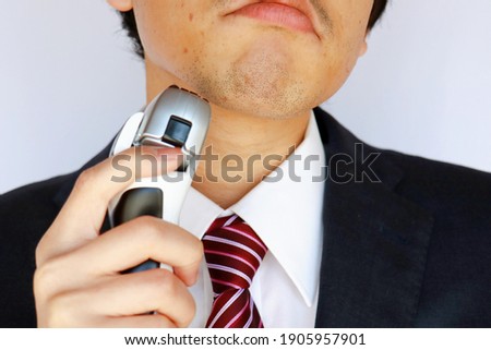 Asian businessman with beard. He's holding an electric shaver.