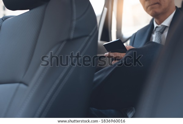 Asian businessman in black suit, executive\
manager using mobile smart phone reading morning news via\
application inside a car on backseat. Corporate man going to\
workplace, people lifestyle\
concept