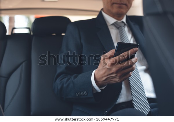 Asian businessman in black suit, executive\
manager using mobile smart phone reading message via application\
inside a car on backseat. Corporate man going to workplace, people\
lifestyle concept