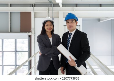 Asian businessman in black suit wearing a blue construction hat,  holding construction drawing. Young female engineer stand next to him. Inspector inspect the orderliness of the factory on the walkway - Shutterstock ID 2207793933
