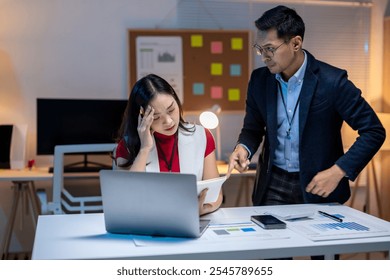 Asian businessman blaming a stressed businesswoman while working together overtime in an office at night - Powered by Shutterstock