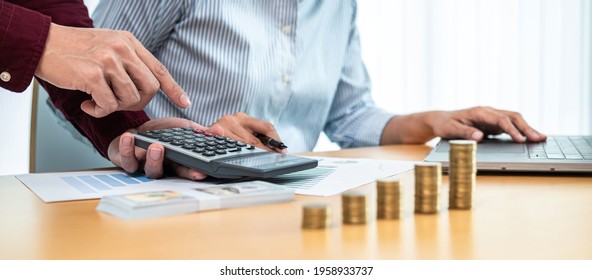 Asian Businessman And Businesswoman Are Working Together To Discussion About House Mortgage And Property Investment While Using Calculator To Calculate Investment Cost With Stack Coins On The Table