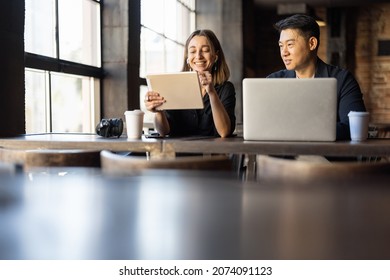 Asian businessman and caucaian business woman working with digital gadgets in cafe or modern office. Concept of remote and freelance work. Idea of teamwork and business cooperation