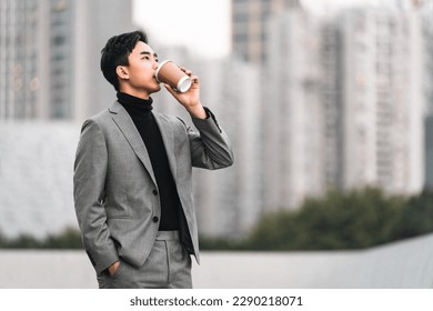 Asian businessman is drinking take away coffee outdoors in the city.  - Powered by Shutterstock