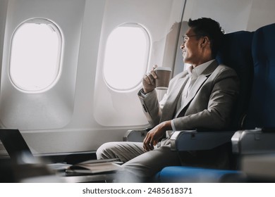 Asian businessman enjoying enjoys a coffee comfortable flight while sitting in the airplane cabin, Passengers near the window. - Powered by Shutterstock