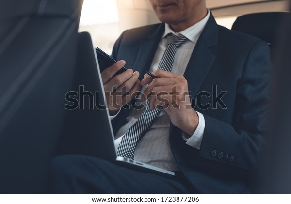 Asian businessman, executive manager taking note via\
mobile phone application, working on laptop computer inside a car,\
portable office, business concept. Corporate man going to\
workplace, close up