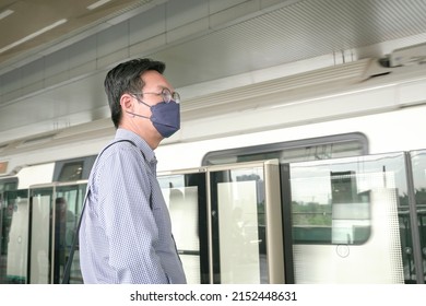 Asian Businessman With Face Mask On Standing On Subway Platform Waiting For Train. Masked Transit Concept.